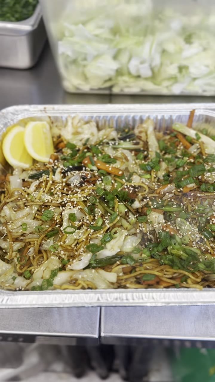 A tray of yakisoba noodles with cabbage and carrot, lemon wedge on top